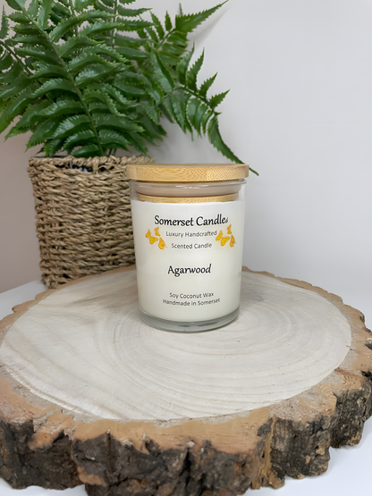 Agarwood soy candle displayed on a wooden board. The candle is white in colour with bright orange butterflies above the scent name with a lovely bamboo lid.