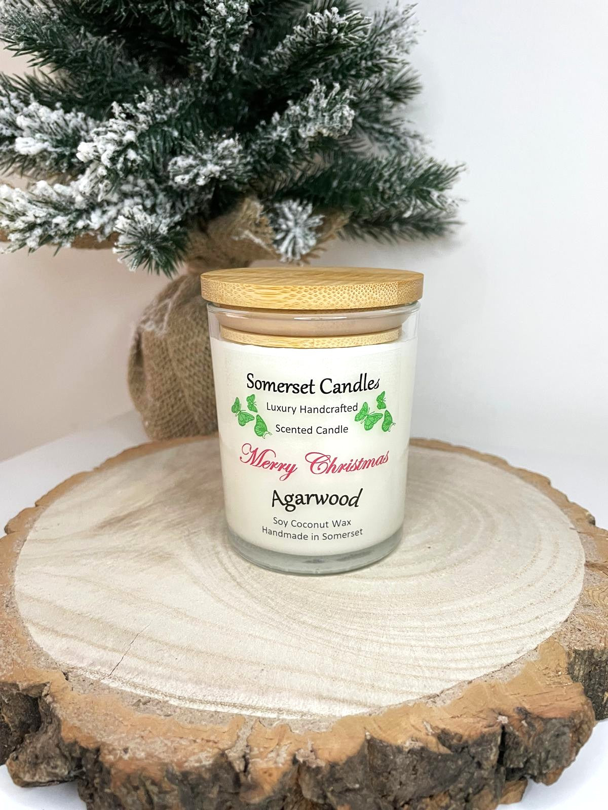 White soy candle in a 7oz clear glass jar with a natural wooden lid. The candle is made from a soy-coconut blend and scented with woodsie scent of agarwood. Above the scent name on the label, several orange butterflies are displayed, adding a romantic touch. Clean, minimalist design ideal for gifts, home decor or self-care.