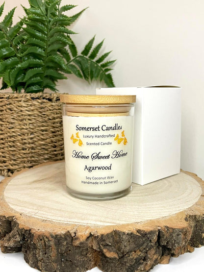 White soy candle in a 7oz clear glass jar with a natural wooden lid. The candle is made from a soy-coconut blend and scented with agarwod. Above the scent name on the label, several Orange butterflies are displayed, adding a romantic touch. Clean, minimalist design ideal for gifts, home decor or self-care.