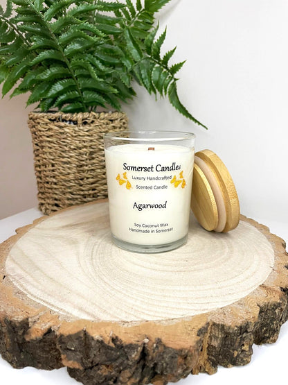 White soy candle in a 7oz clear glass jar with a natural wooden lid. The candle is made from a soy-coconut blend and scented with woodsie scent of agarwood. Above the scent name on the label, several orange butterflies are displayed, adding a romantic touch. Clean, minimalist design ideal for gifts, home decor or self-care.