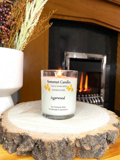 White soy candle in a 7oz clear glass jar with a natural wooden lid. The candle is made from a soy-coconut blend and scented with woodsie scent of agarwood. Above the scent name on the label, several orange butterflies are displayed, adding a romantic touch. Clean, minimalist design ideal for gifts, home decor or self-care.