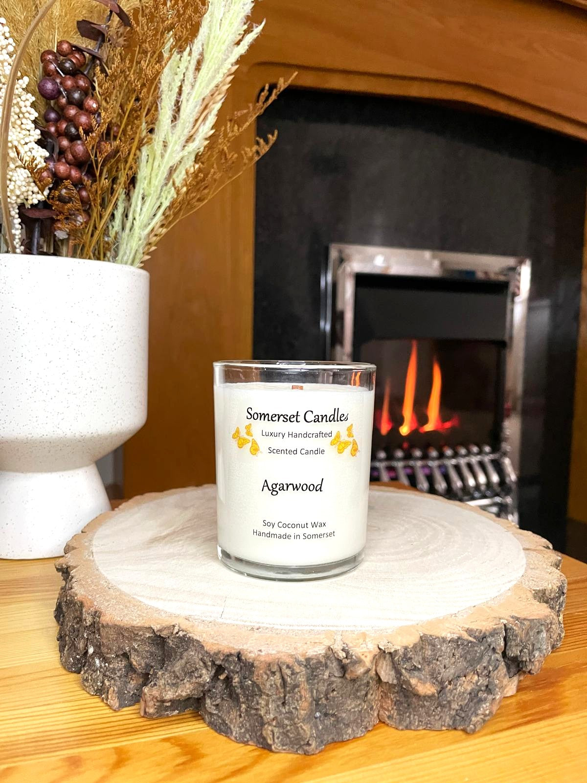 White soy candle in a 7oz clear glass jar with a natural wooden lid. The candle is made from a soy-coconut blend and scented with woodsie scent of agarwood. Above the scent name on the label, several orange butterflies are displayed, adding a romantic touch. Clean, minimalist design ideal for gifts, home decor or self-care.