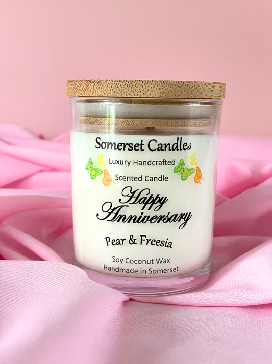 Somerset Candles 'Happy Anniversary' scented candle with a wooden lid on a pink fabric background