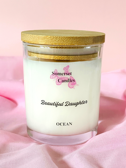 Somerset Candles 'Beautiful Daughter' ocean-scented candle on a pink fabric background