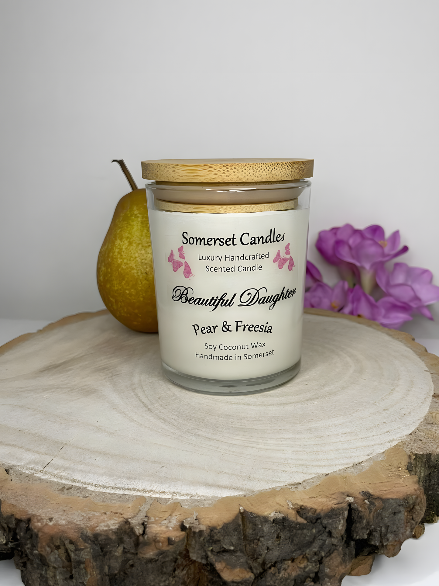 Beautiful Daughter Pear & Freesia scented soy candle is displayed with fresh pear & freesia. The candle is white in colour with bright pink butterflies fluttering above the scent name and fitted with a lovely bamboo lid.