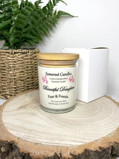 White soy candle in a 7oz clear glass jar with a natural wooden lid. The candle is made from a soy-coconut blend and scented with a delicate mix of pear and freesia. Above the scent name on the label, several pink butterflies are displayed, adding a romantic touch. Clean, minimalist design ideal for gifts, home decor or self-care.