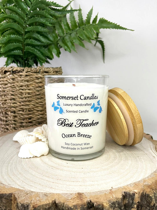 White soy candle in a 7oz clear glass jar with a natural wooden lid. The candle is made from a soy-coconut blend and scented with a fresh scent of ocean breeze. Above the scent name on the label, several blue butterflies are displayed, adding a romantic touch. Clean, minimalist design ideal for gifts, home decor or self-care.