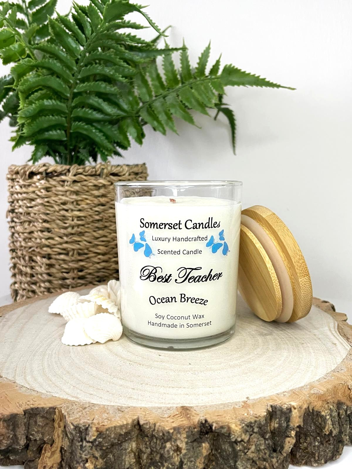 White soy candle in a 7oz clear glass jar with a natural wooden lid. The candle is made from a soy-coconut blend and scented with a fresh scent of ocean breeze. Above the scent name on the label, several blue butterflies are displayed, adding a romantic touch. Clean, minimalist design ideal for gifts, home decor or self-care.