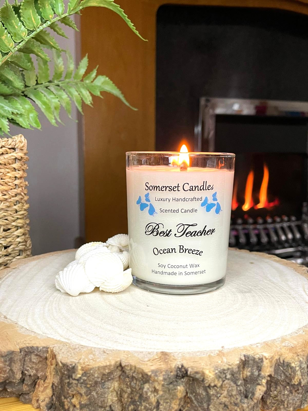 White soy candle in a 7oz clear glass jar with a natural wooden lid. The candle is made from a soy-coconut blend and scented with a fresh scent of ocean breeze. Above the scent name on the label, several blue butterflies are displayed, adding a romantic touch. Clean, minimalist design ideal for gifts, home decor or self-care.