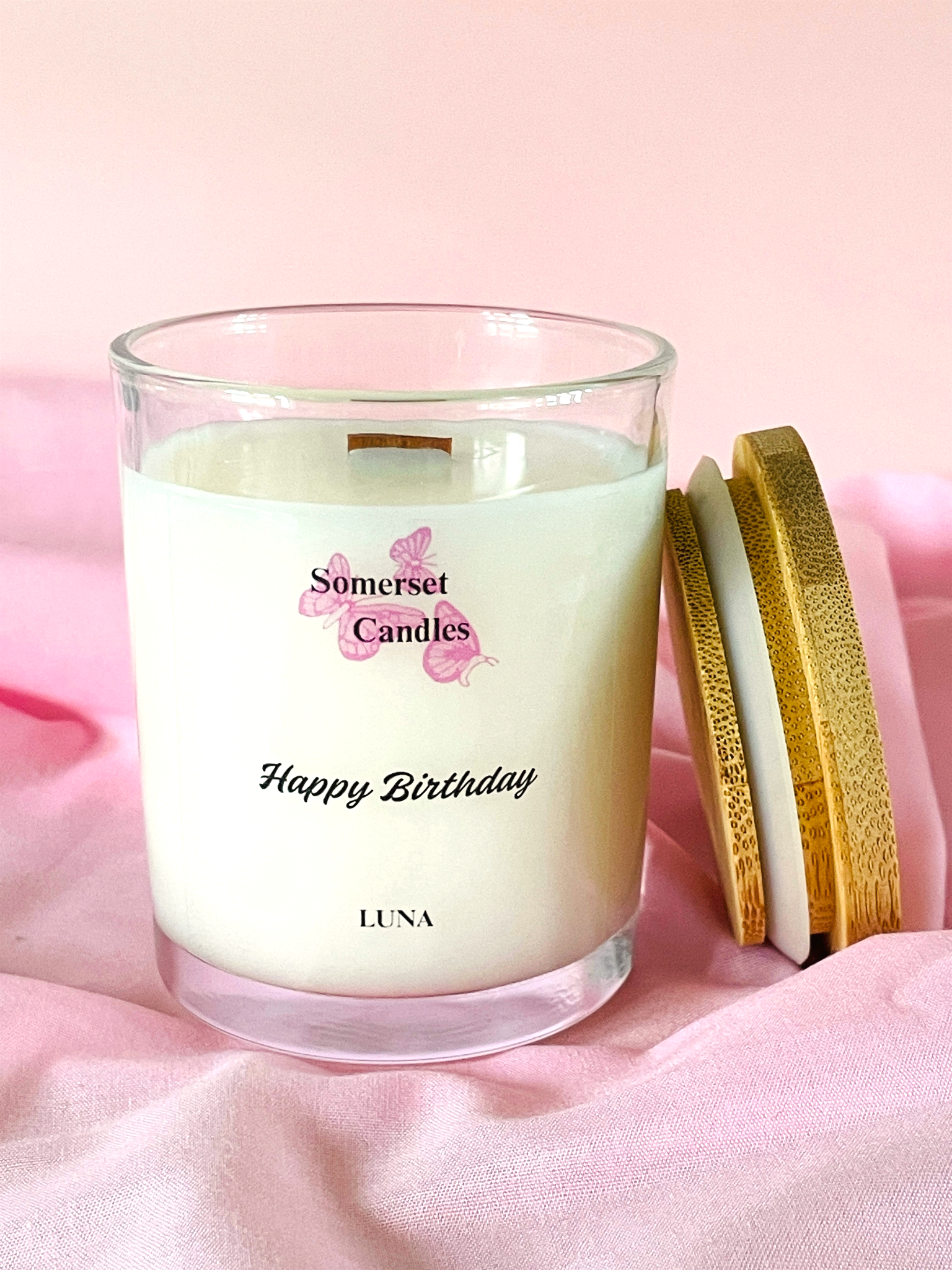 Somerset Candles 'Happy Birthday Luna' candle on a pink fabric background
