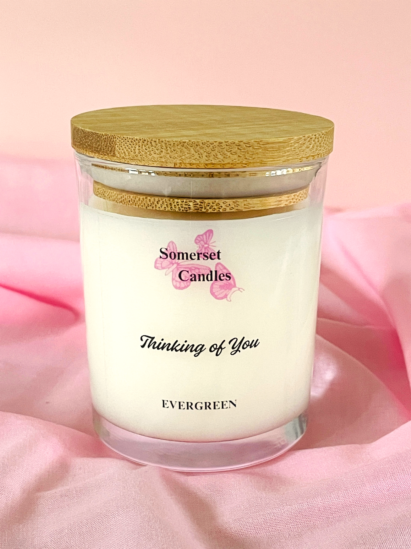 Candle jar with wooden lid on a pink fabric background, featuring 'Somerset Candles' branding.