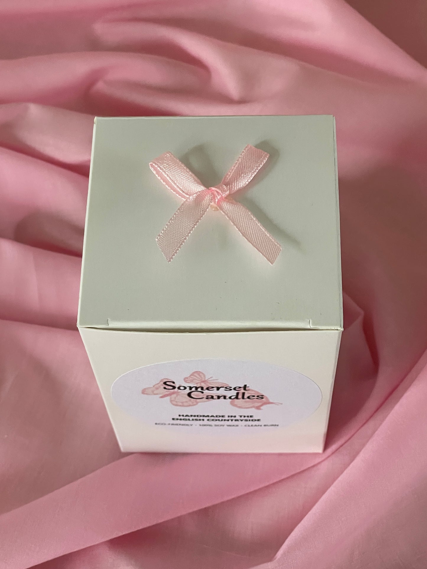 White gift box with a pink ribbon on a pink fabric background