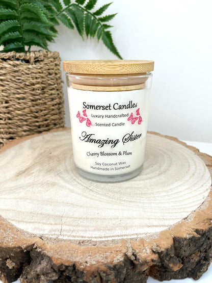 White soy candle in a 7oz clear glass jar with a natural wooden lid. The candle is made from a soy-coconut blend and scented with a delicate mix of cherry blossom and plum. Above the scent name on the label, several red butterflies are displayed, adding a romantic touch. Clean, minimalist design ideal for gifts, home decor or self-care.