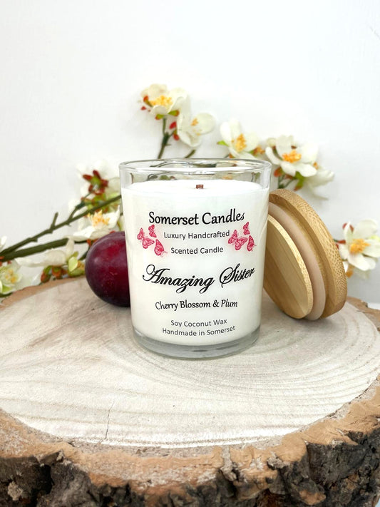 White soy candle in a 7oz clear glass jar with a natural wooden lid. The candle is made from a soy-coconut blend and scented with a delicate mix of cherry blossom and plum. Above the scent name on the label, several red butterflies are displayed, adding a romantic touch. Clean, minimalist design ideal for gifts, home decor or self-care.