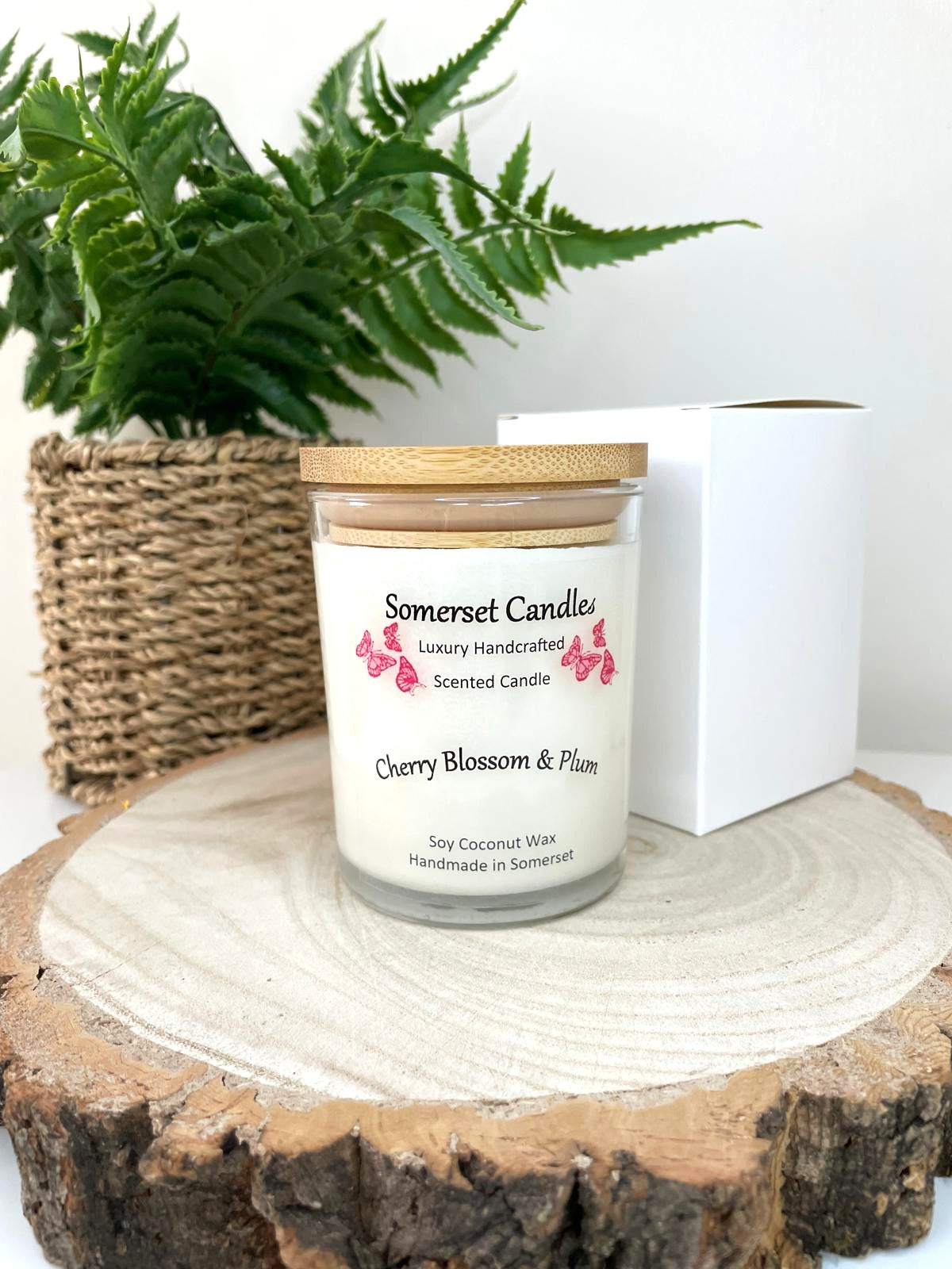 White soy candle in a 7oz clear glass jar with a natural wooden lid. The candle is made from a soy-coconut blend and scented with a delicate mix of cherry blossom and plum. Above the scent name on the label, several red butterflies are displayed, adding a romantic touch. Clean, minimalist design ideal for gifts, home decor or self-care.