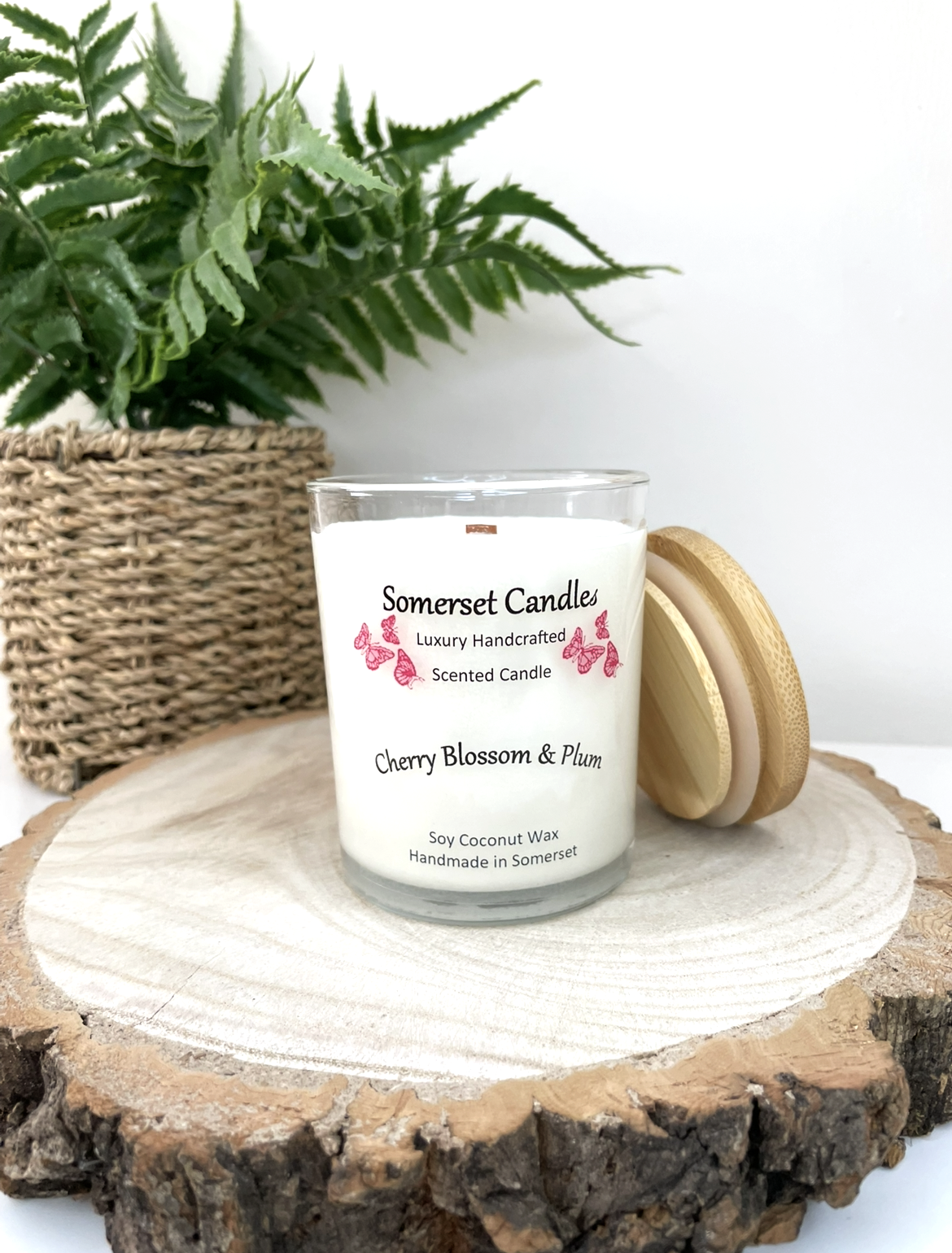 White soy candle in a 7oz clear glass jar with a natural wooden lid. The candle is made from a soy-coconut blend and scented with a delicate mix of cherry blossom and plum. Above the scent name on the label, several red butterflies are displayed, adding a romantic touch. Clean, minimalist design ideal for gifts, home decor or self-care.