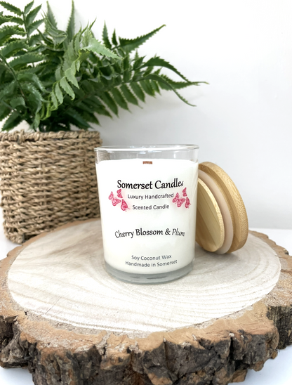 White soy candle in a 7oz clear glass jar with a natural wooden lid. The candle is made from a soy-coconut blend and scented with a delicate mix of cherry blossom and plum. Above the scent name on the label, several red butterflies are displayed, adding a romantic touch. Clean, minimalist design ideal for gifts, home decor or self-care.