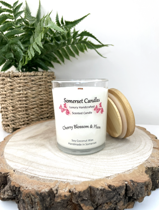 White soy candle in a 7oz clear glass jar with a natural wooden lid. The candle is made from a soy-coconut blend and scented with a delicate mix of cherry blossom and plum. Above the scent name on the label, several red butterflies are displayed, adding a romantic touch. Clean, minimalist design ideal for gifts, home decor or self-care.