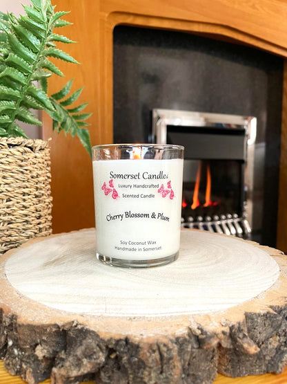 White soy candle in a 7oz clear glass jar with a natural wooden lid. The candle is made from a soy-coconut blend and scented with a delicate mix of cherry blossom and plum. Above the scent name on the label, several red butterflies are displayed, adding a romantic touch. Clean, minimalist design ideal for gifts, home decor or self-care.