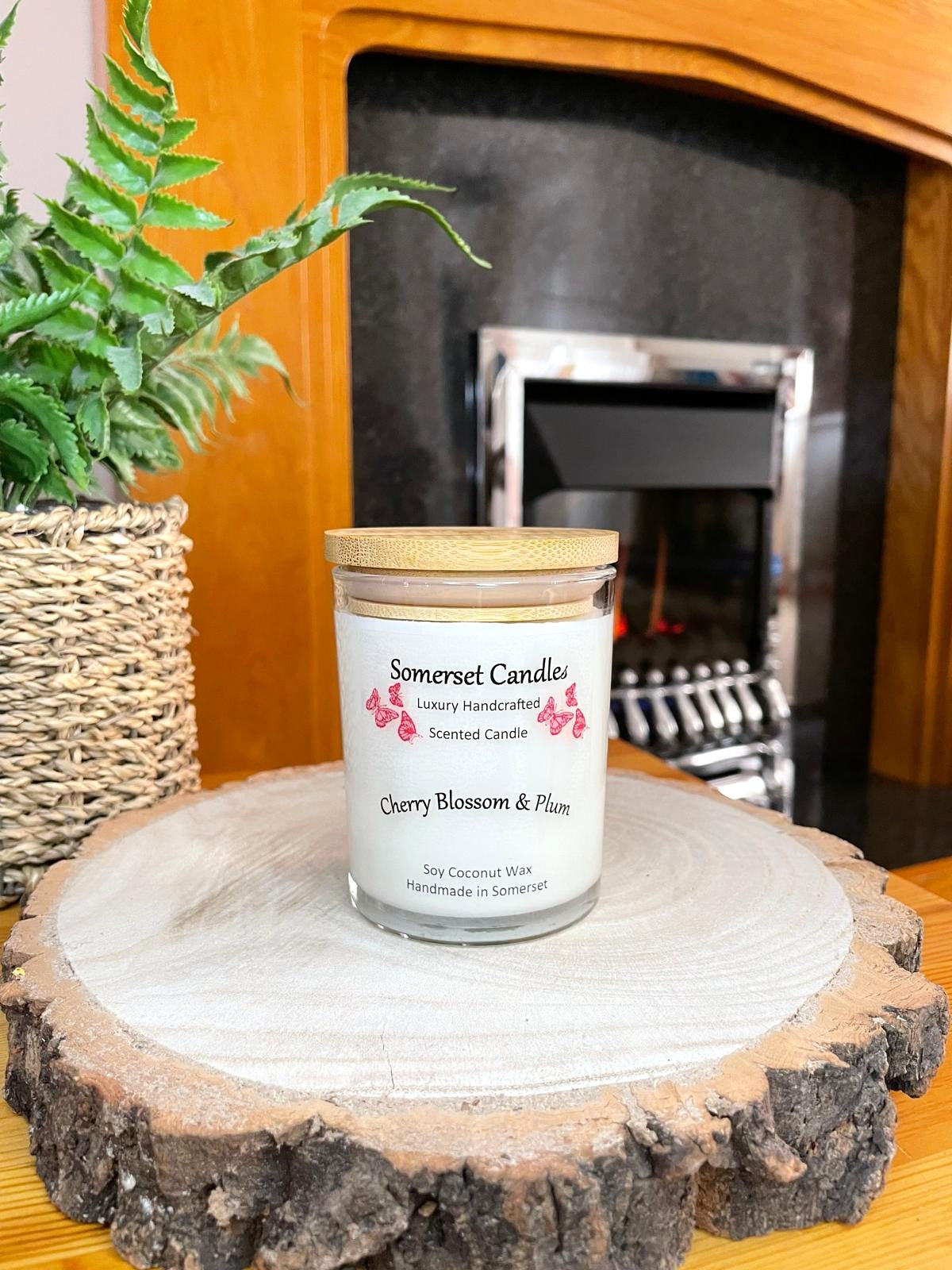 White soy candle in a 7oz clear glass jar with a natural wooden lid. The candle is made from a soy-coconut blend and scented with a delicate mix of cherry blossom and plum. Above the scent name on the label, several red butterflies are displayed, adding a romantic touch. Clean, minimalist design ideal for gifts, home decor or self-care.