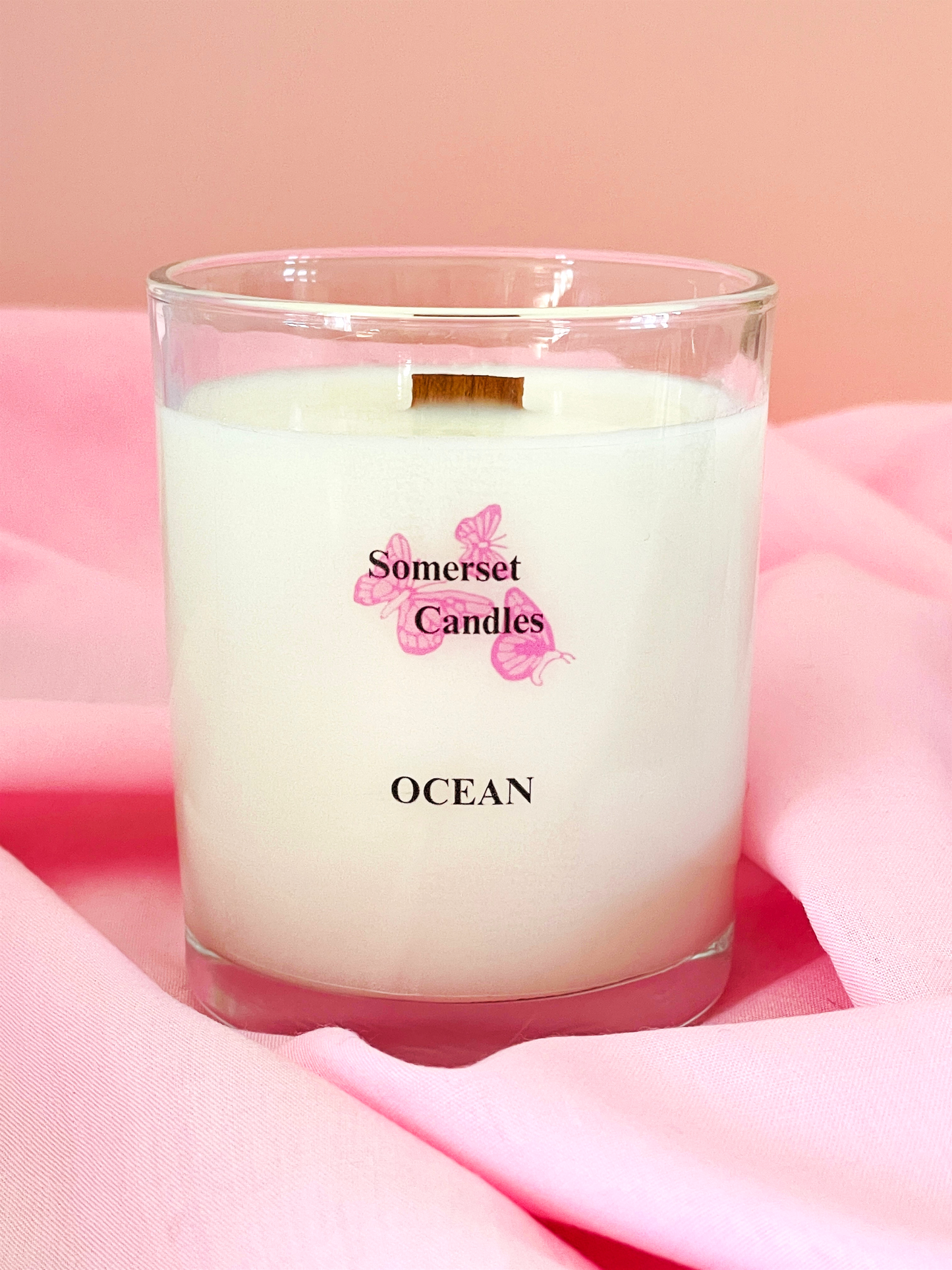 Candle labeled 'Somerset Candles Ocean' on a pink fabric background