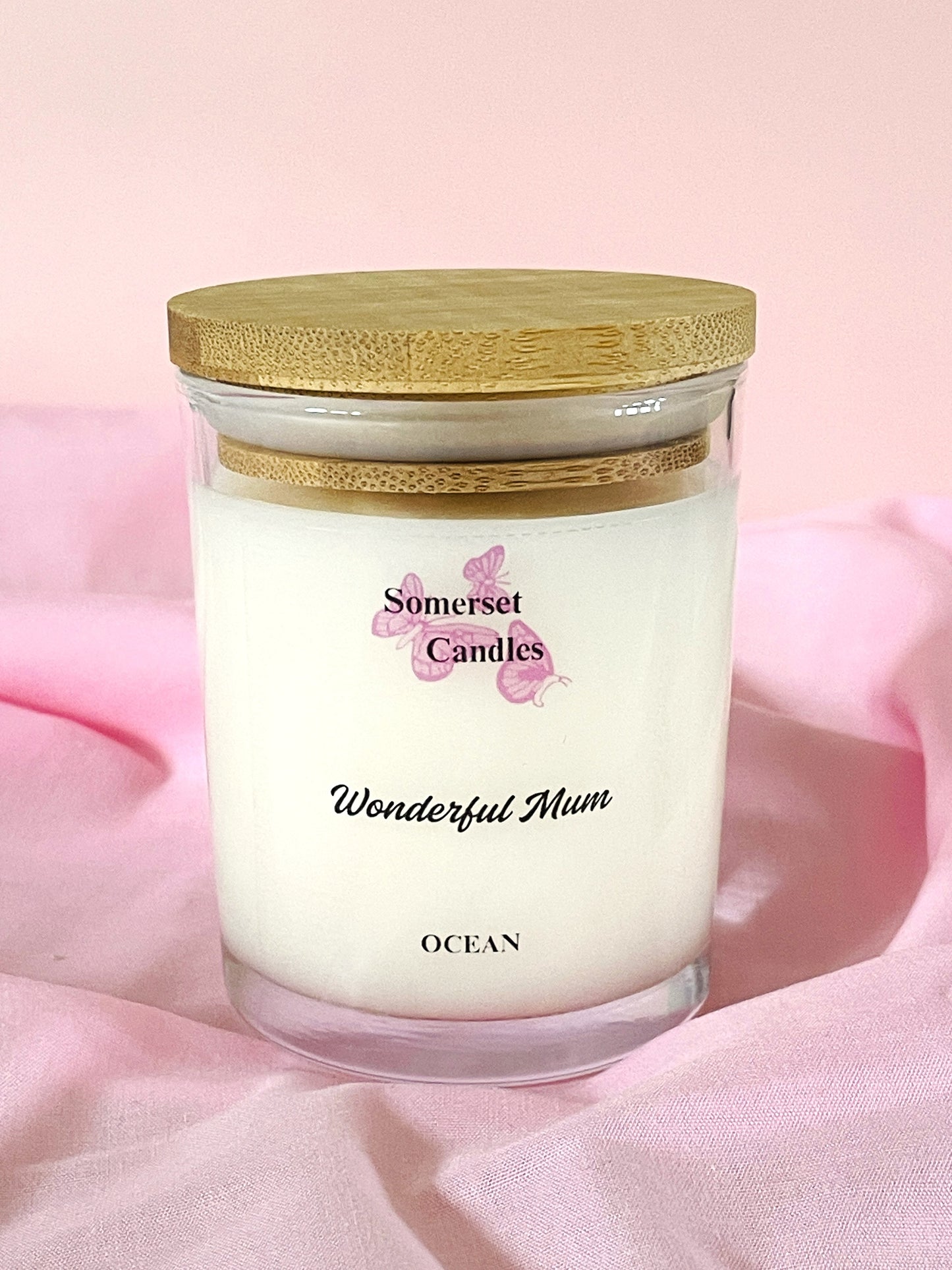 Somerset Candles 'Wonderful Mum' ocean-scented candle with a bamboo lid on a pink fabric background