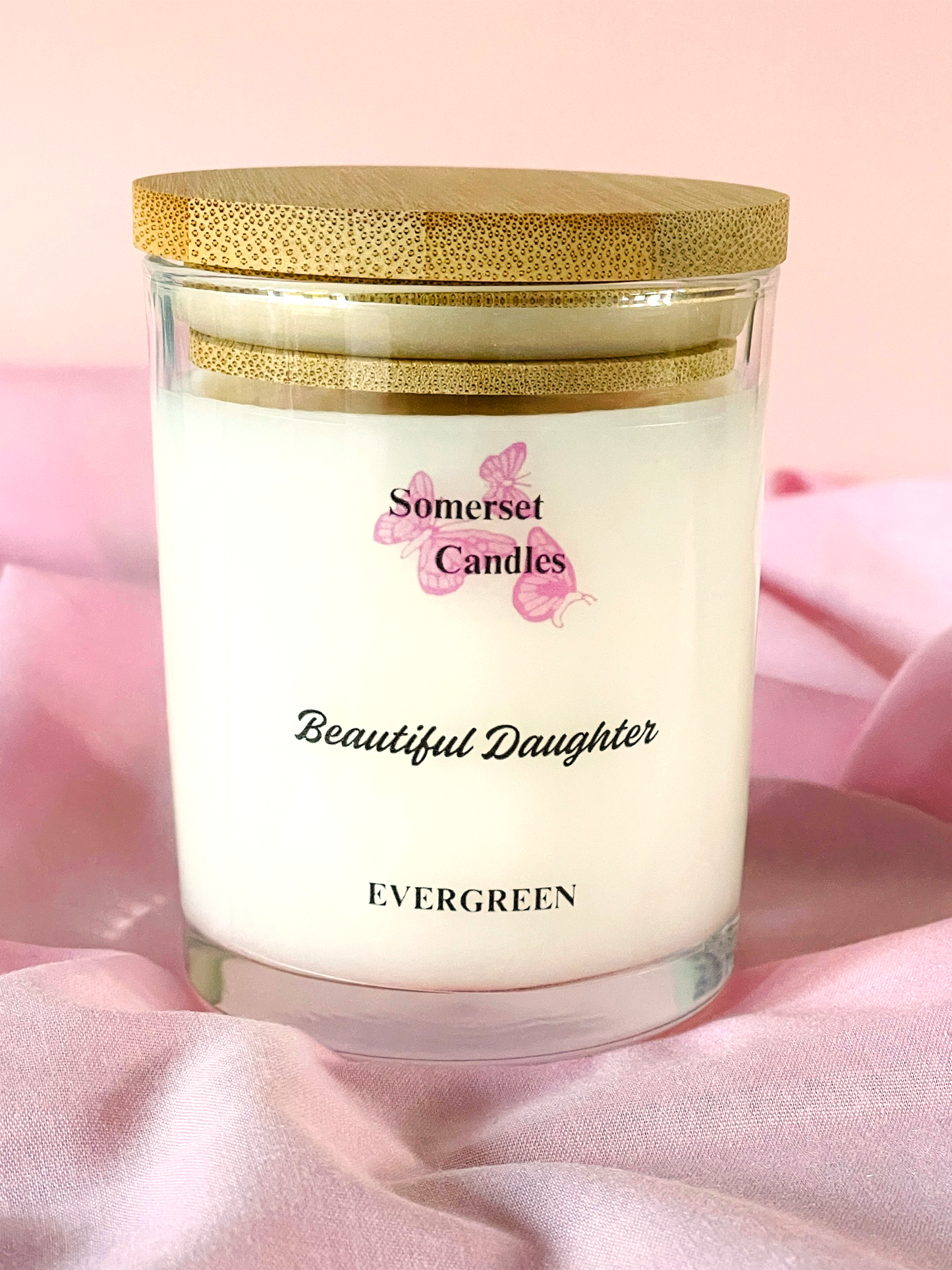 Somerset Candles 'Beautiful Daughter' candle with a gold lid on a pink fabric background