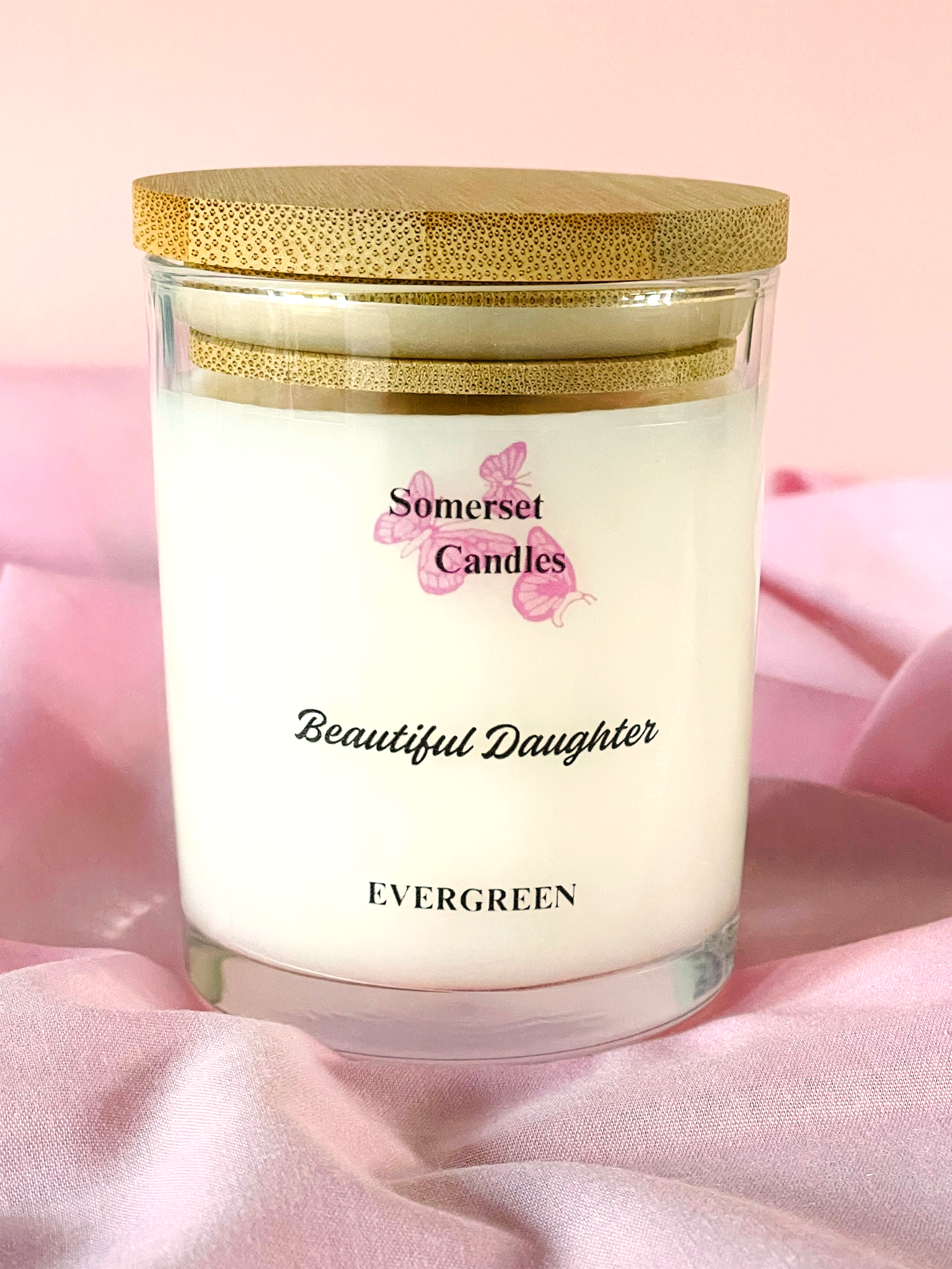 Somerset Candles 'Beautiful Daughter' candle with a wooden lid on a pink fabric background
