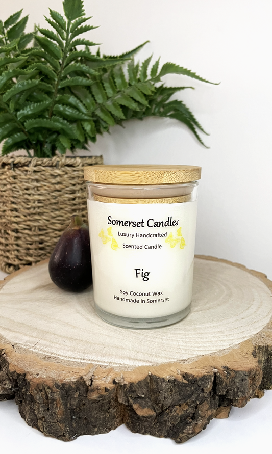 White soy candle in a 7oz clear glass jar with a natural wooden lid. The candle is made from a soy-coconut blend and scented with a fresh scent of ripe fig. Above the scent name on the label, several yellow butterflies are displayed, adding a romantic touch. Clean, minimalist design ideal for gifts, home decor or self-care.