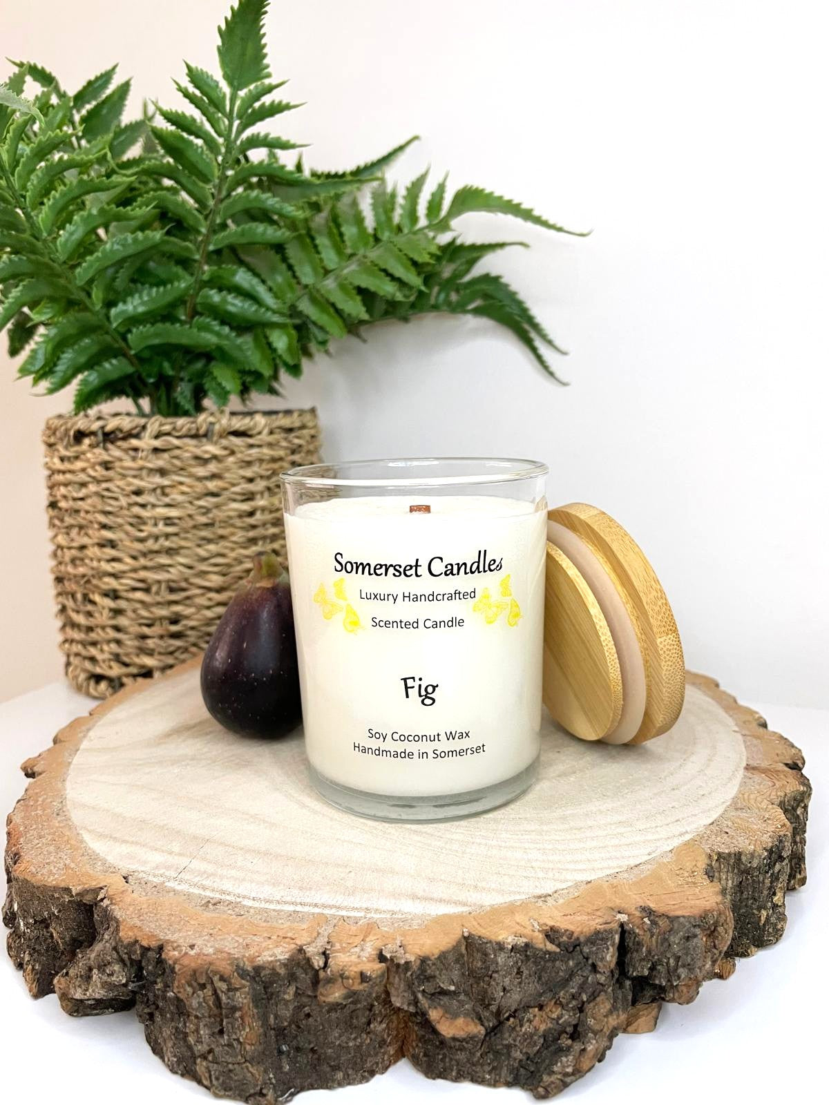 White soy candle in a 7oz clear glass jar with a natural wooden lid. The candle is made from a soy-coconut blend and scented with a fresh scent of ripe fig. Above the scent name on the label, several yellow butterflies are displayed, adding a romantic touch. Clean, minimalist design ideal for gifts, home decor or self-care.
