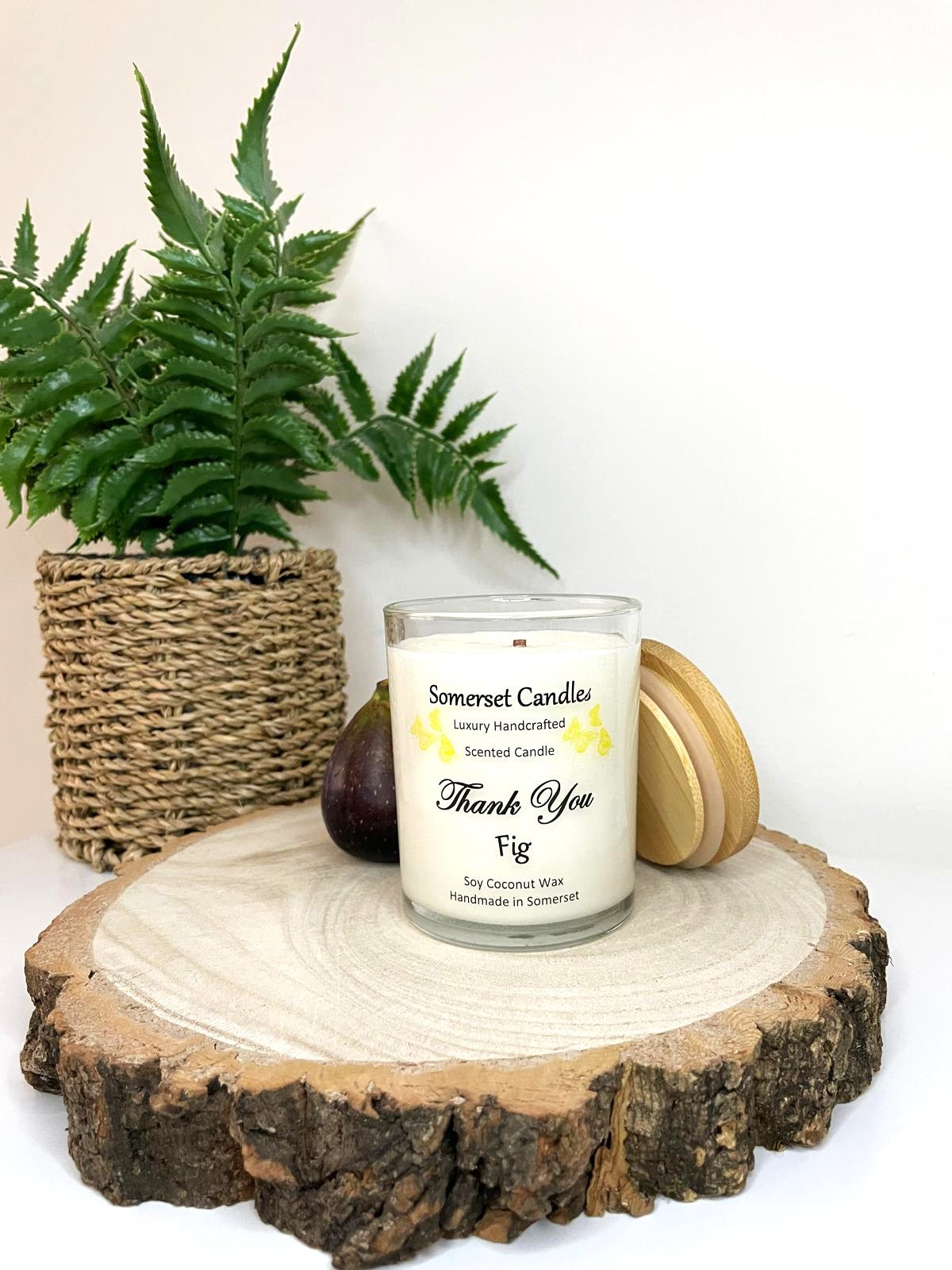 White soy candle in a 7oz clear glass jar with a natural wooden lid. The candle is made from a soy-coconut blend and scented with ripe fig. Above the scent name on the label, several yellow butterflies are displayed, adding a romantic touch. Clean, minimalist design ideal for gifts, home decor or self-care.