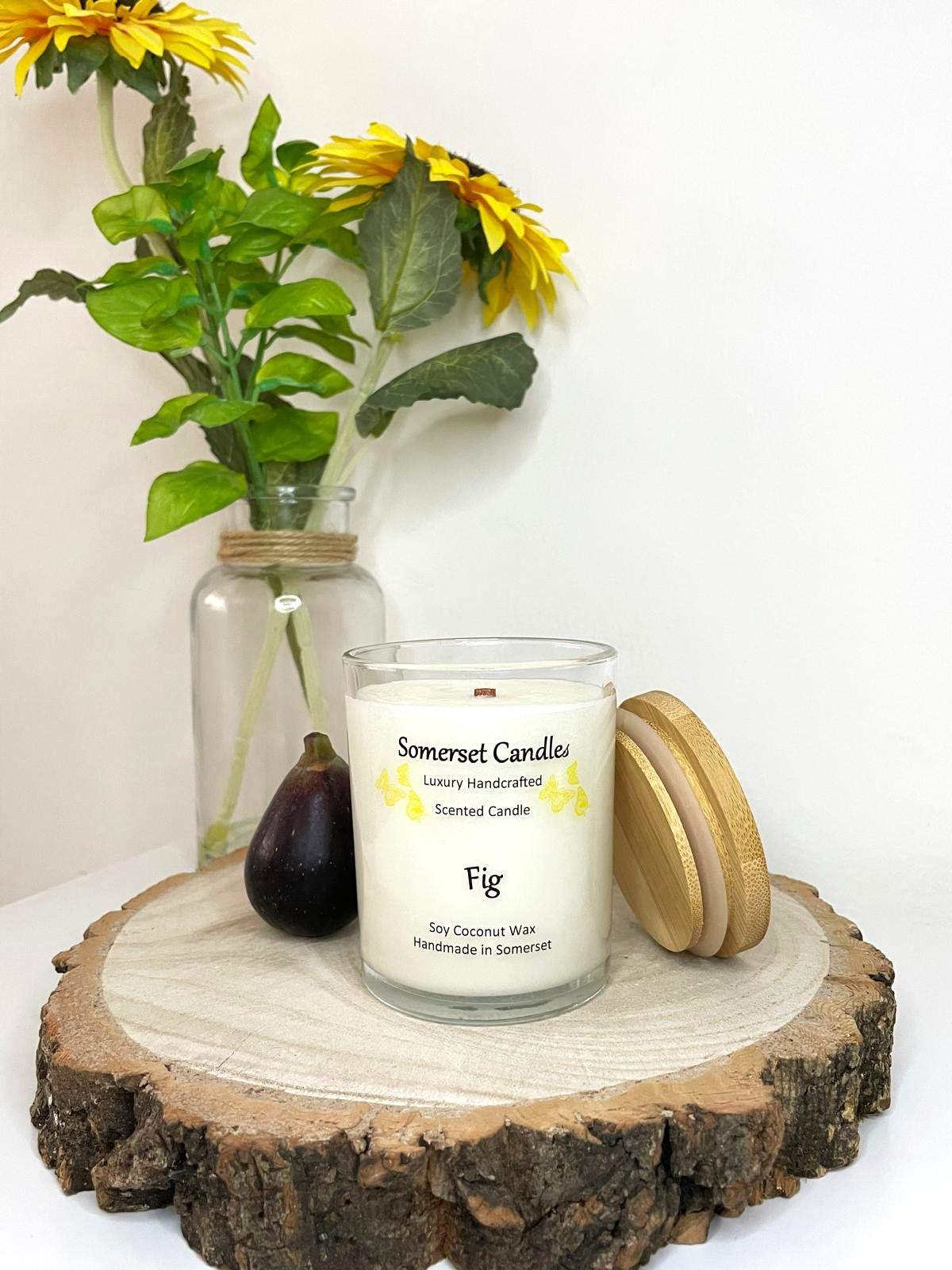White soy candle in a 7oz clear glass jar with a natural wooden lid. The candle is made from a soy-coconut blend and scented with a fresh scent of ripe fig. Above the scent name on the label, several yellow butterflies are displayed, adding a romantic touch. Clean, minimalist design ideal for gifts, home decor or self-care.