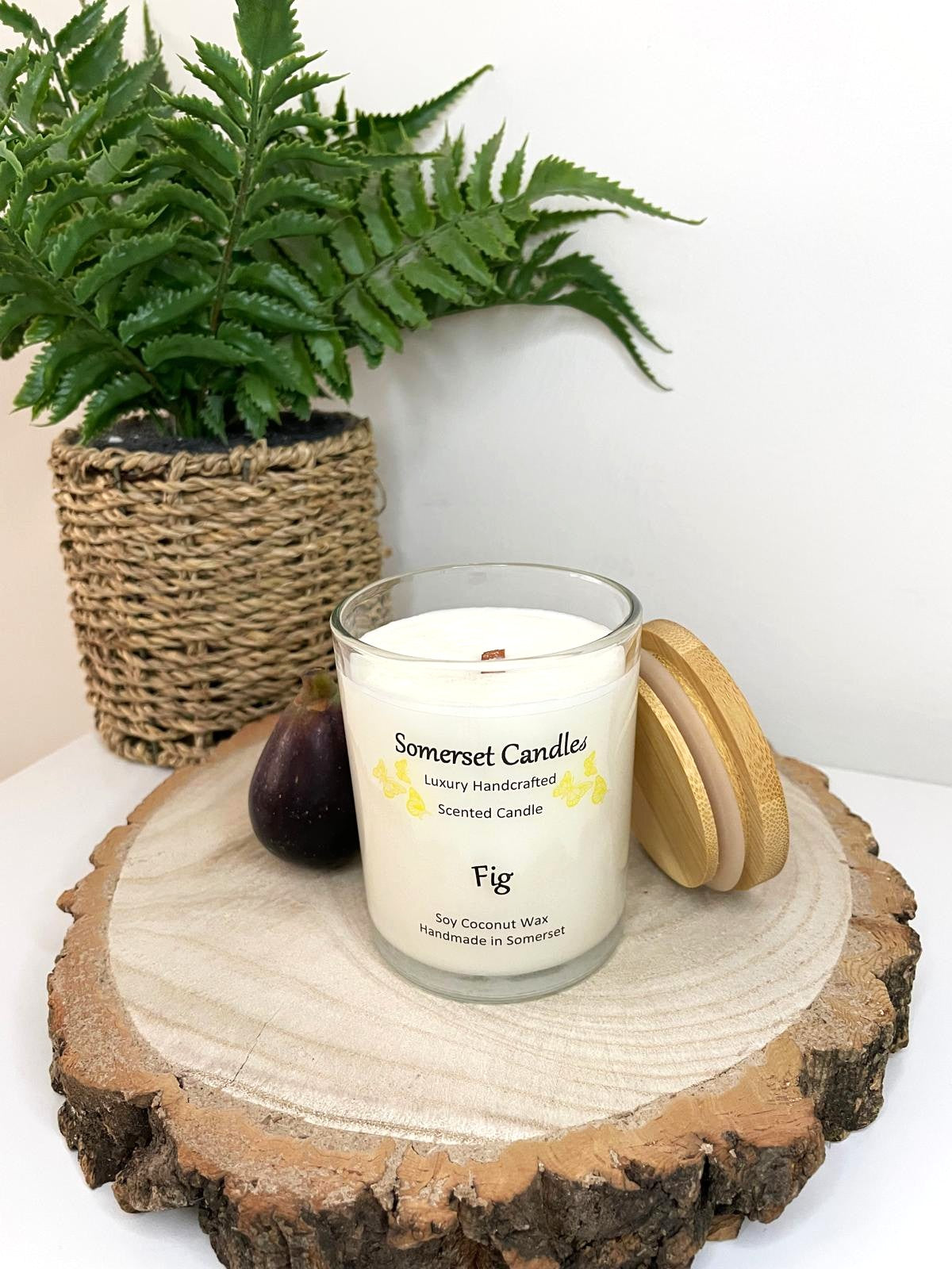White soy candle in a 7oz clear glass jar with a natural wooden lid. The candle is made from a soy-coconut blend and scented with a fresh scent of ripe fig. Above the scent name on the label, several yellow butterflies are displayed, adding a romantic touch. Clean, minimalist design ideal for gifts, home decor or self-care.