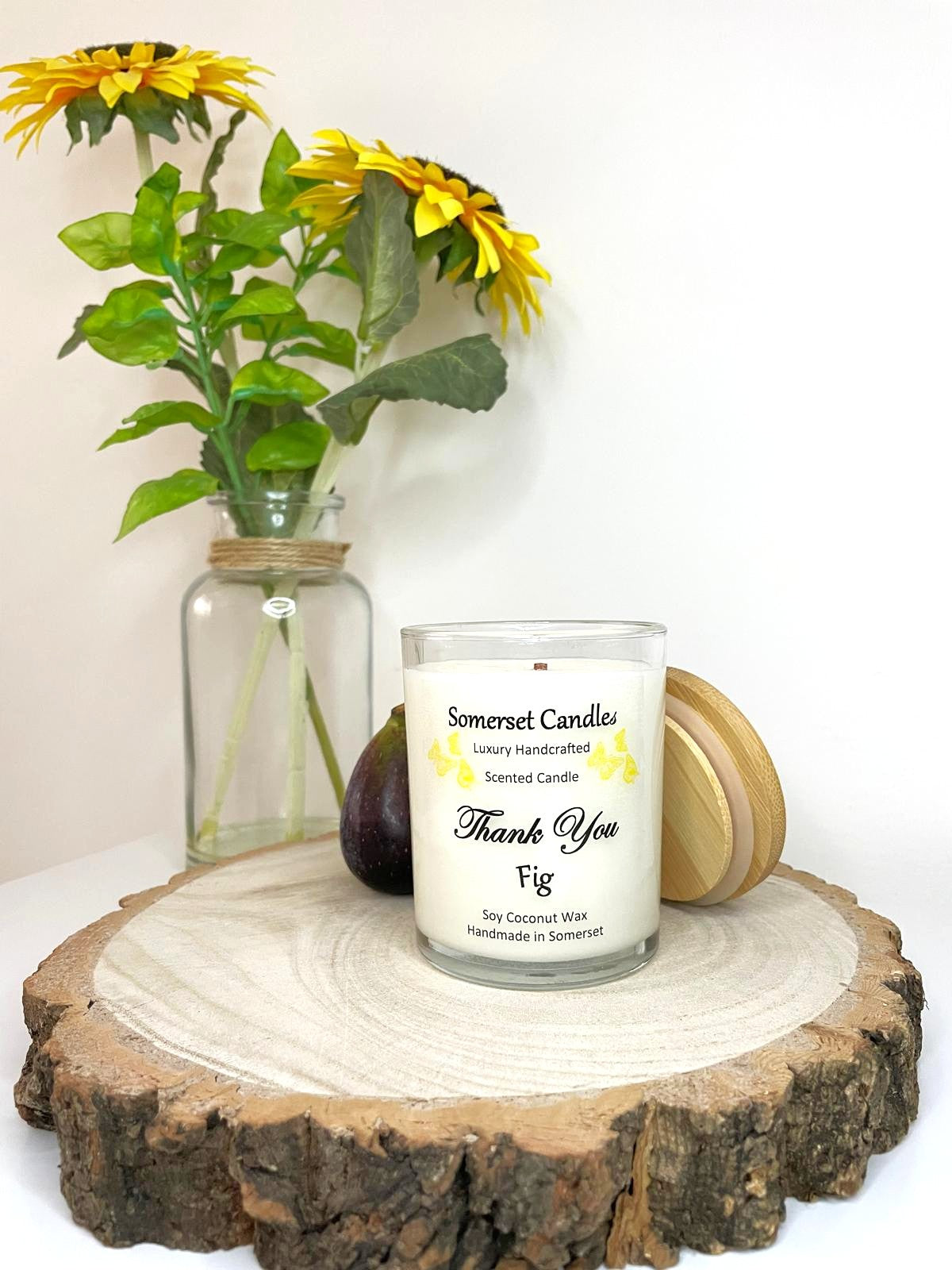 White soy candle in a 7oz clear glass jar with a natural wooden lid. The candle is made from a soy-coconut blend and scented with ripe fig. Above the scent name on the label, several yellow butterflies are displayed, adding a romantic touch. Clean, minimalist design ideal for gifts, home decor or self-care.