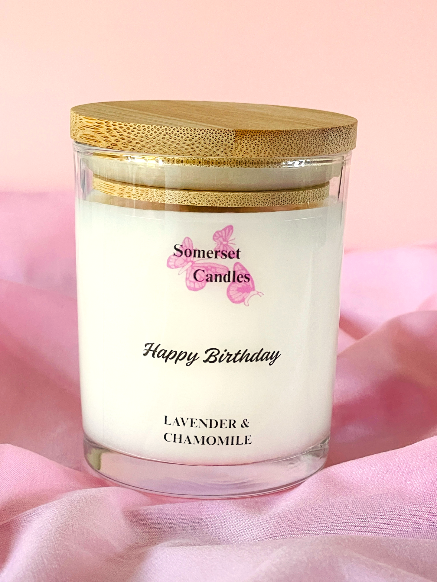 Candle with a wooden lid labeled 'Somerset Candles' on a pink background