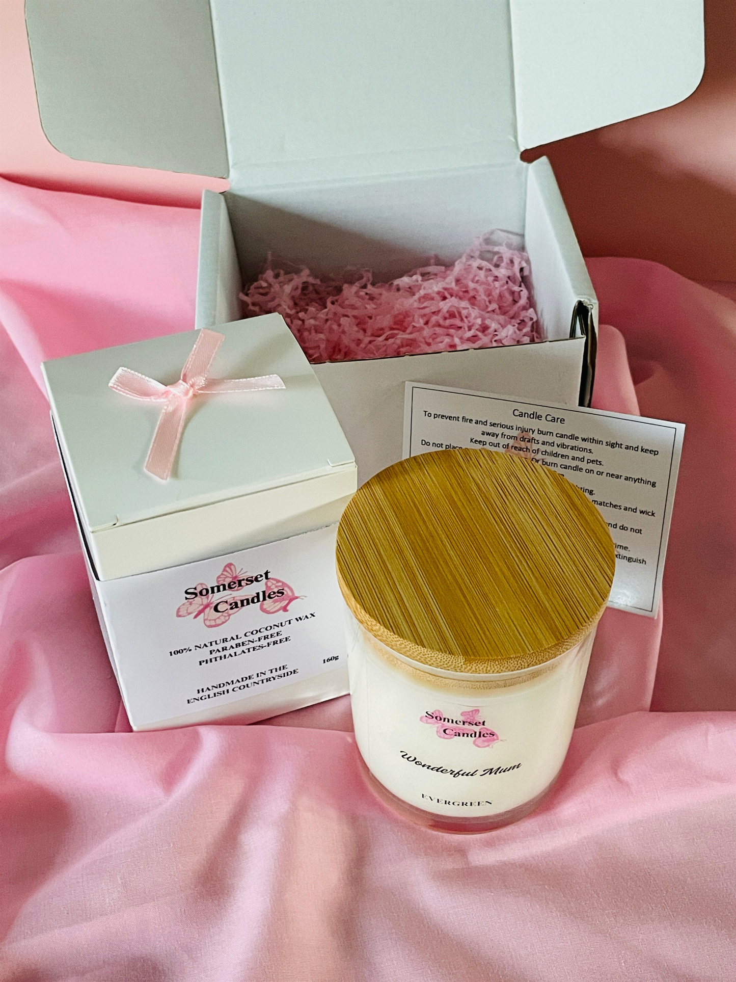Candle in a box with a wooden lid on a pink fabric background