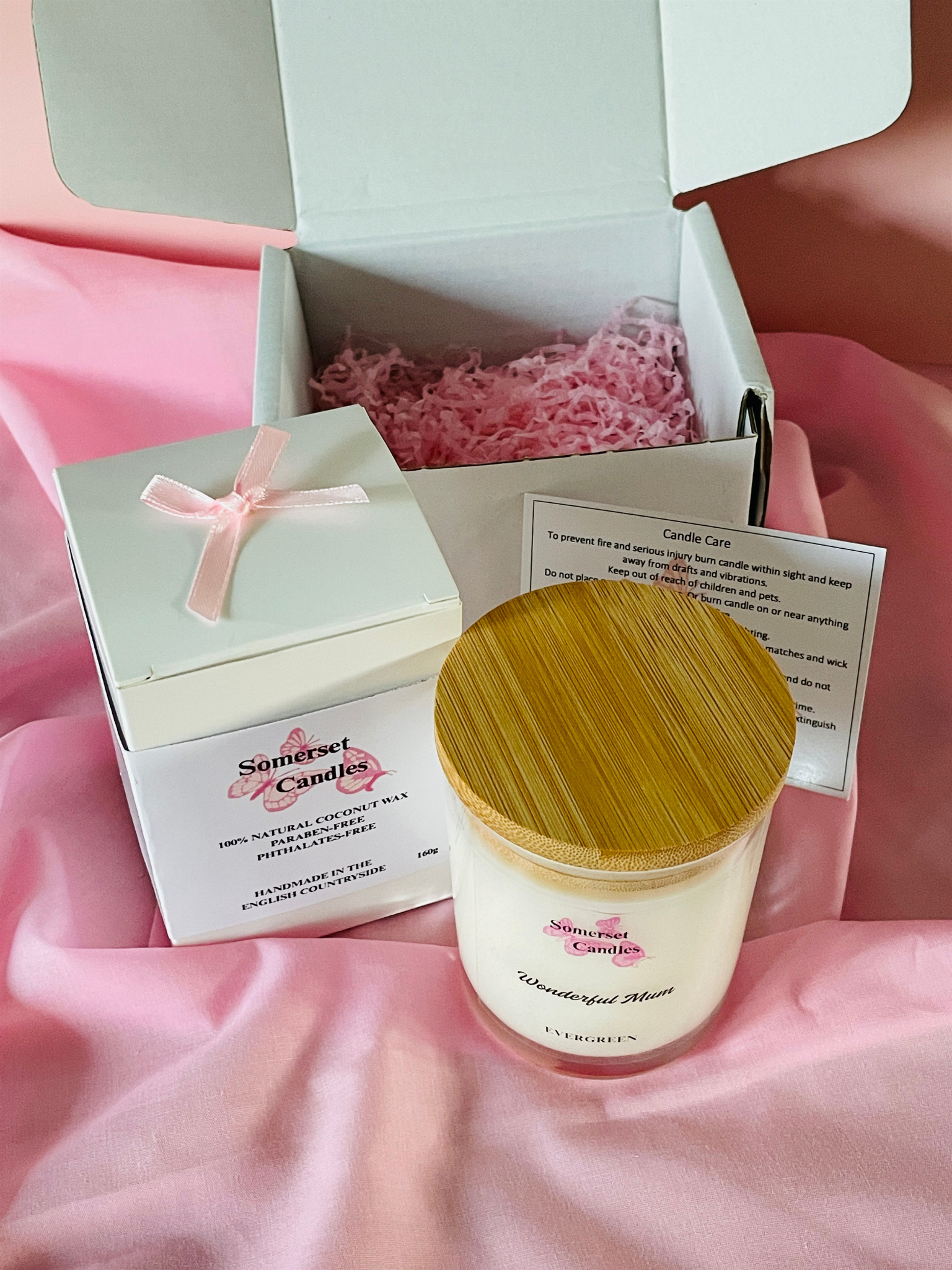 Candle in a box with a wooden lid on a pink fabric background