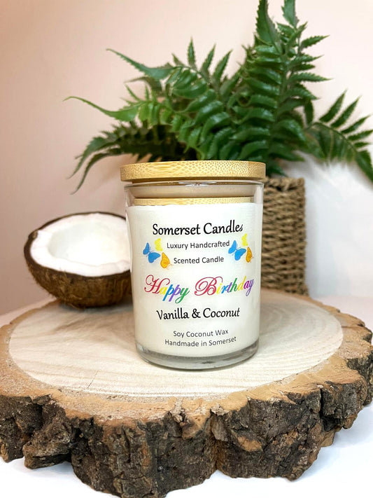 White soy candle in a 7oz clear glass jar with a natural wooden lid. The candle is made from a soy-coconut blend and scented with vanilla and coconut. Above the scent name on the label, several yellow, orange and blue butterflies are displayed, adding a romantic touch. Clean, minimalist design ideal for gifts, home decor or self-care.
