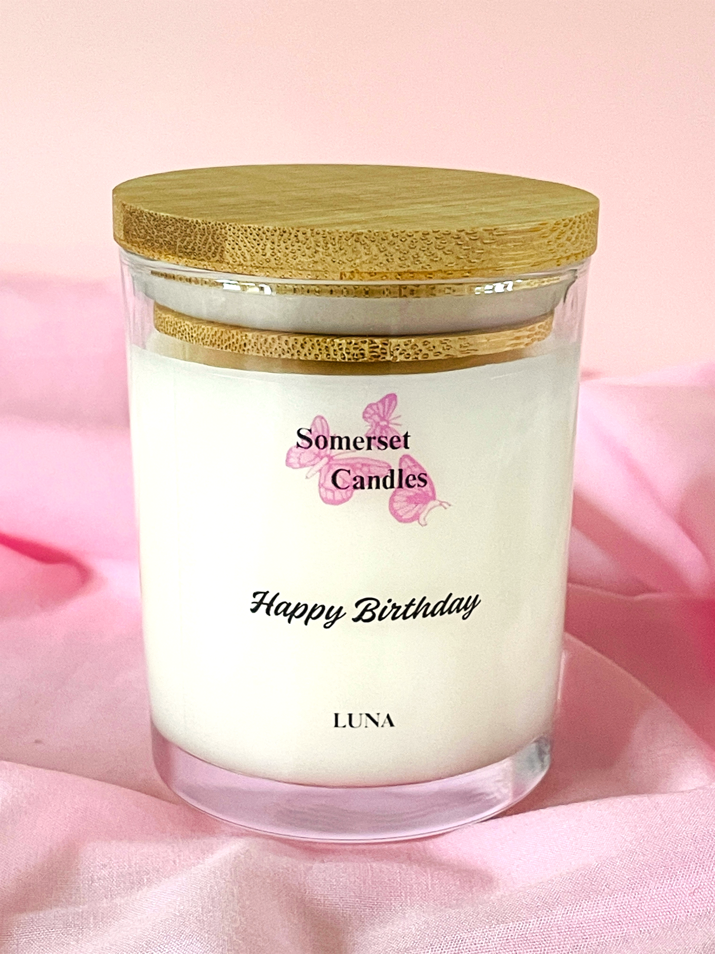 Somerset Candles 'Happy Birthday Luna' candle with a wooden lid on a pink background