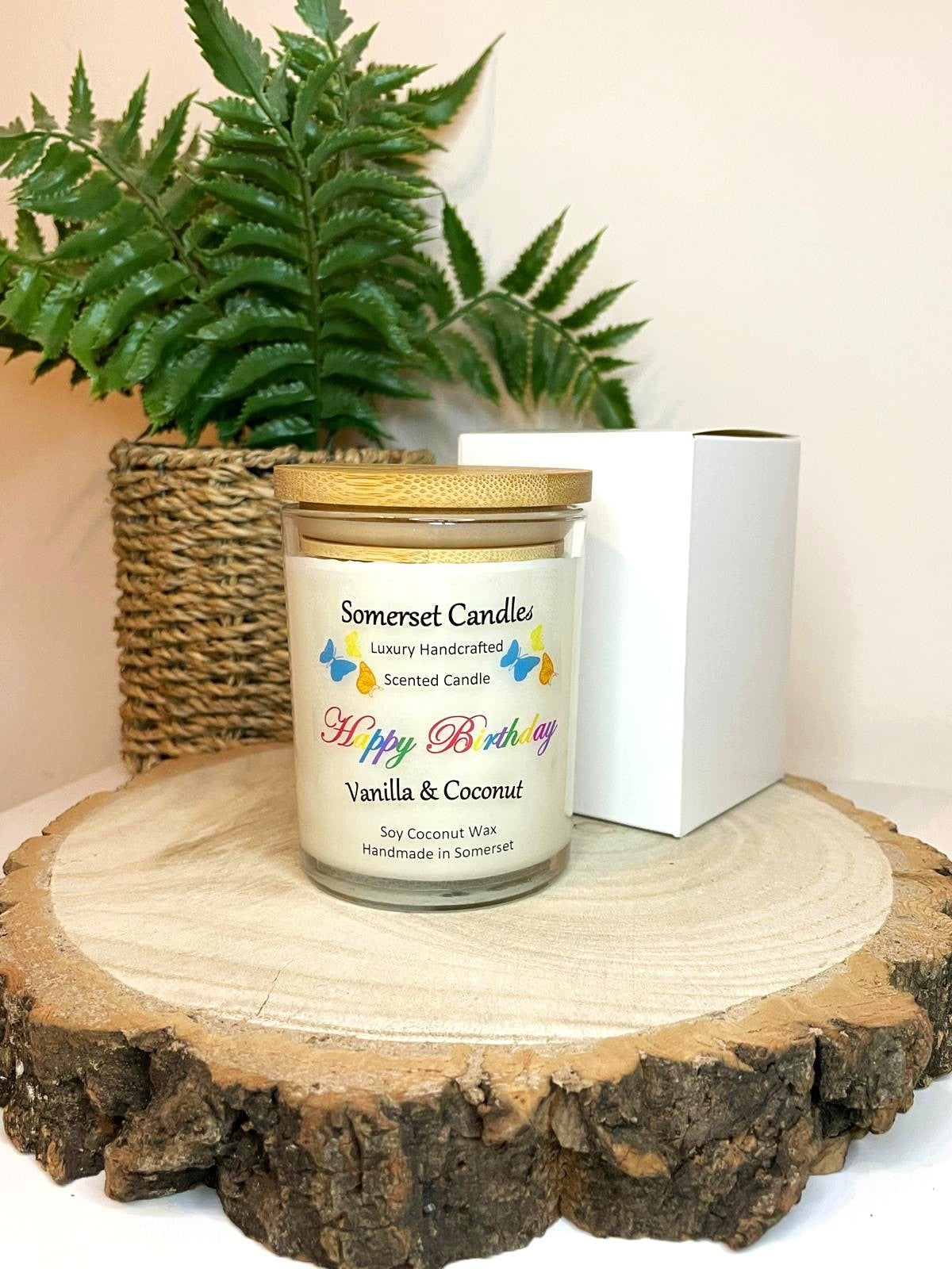 White soy candle in a 7oz clear glass jar with a natural wooden lid. The candle is made from a soy-coconut blend and scented with vanilla and coconut. Above the scent name on the label, several yellow, orange and blue butterflies are displayed, adding a romantic touch. Clean, minimalist design ideal for gifts, home decor or self-care.