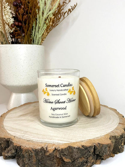 White soy candle in a 7oz clear glass jar with a natural wooden lid. The candle is made from a soy-coconut blend and scented with agarwod. Above the scent name on the label, several Orange butterflies are displayed, adding a romantic touch. Clean, minimalist design ideal for gifts, home decor or self-care.
