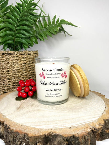 White soy candle in a 7oz clear glass jar with a natural wooden lid. The candle is made from a soy-coconut blend and scented with fruity winter berries. Above the scent name on the label, several red butterflies are displayed, adding a romantic touch. Clean, minimalist design ideal for gifts, home decor or self-care.
