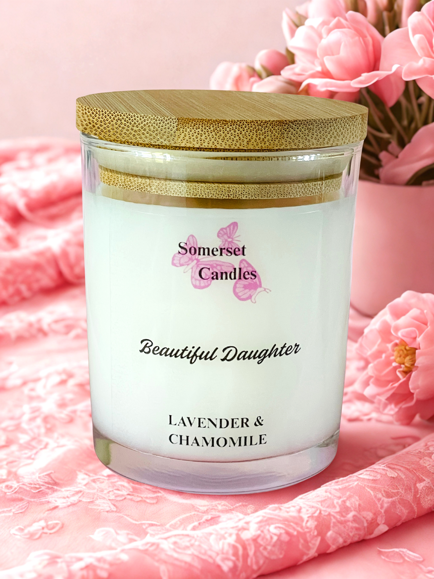 Somerset Candles 'Beautiful Daughter' lavender and chamomile candle on a pink textured surface with flowers in the background.