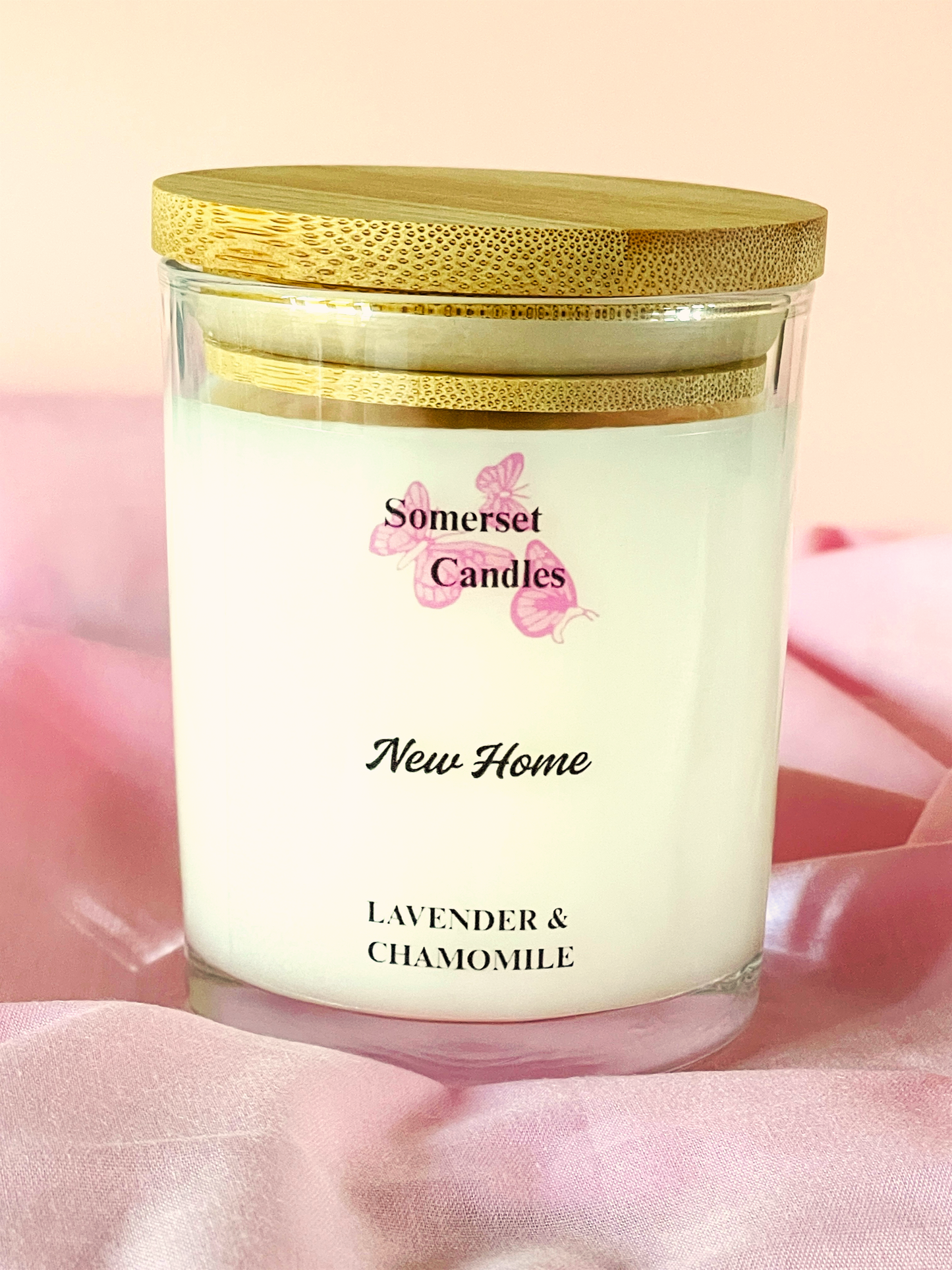 Scented candle in a glass jar with a gold lid on a pink fabric background, featuring 'Somerset Candles' branding.