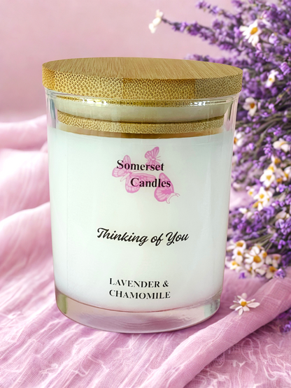 Somerset Candles 'Thinking of You' lavender and chamomile candle with a wooden lid on a pink fabric background.