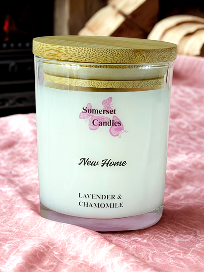 Scented candle labeled 'New Home' by Somerset Candles on a pink surface.