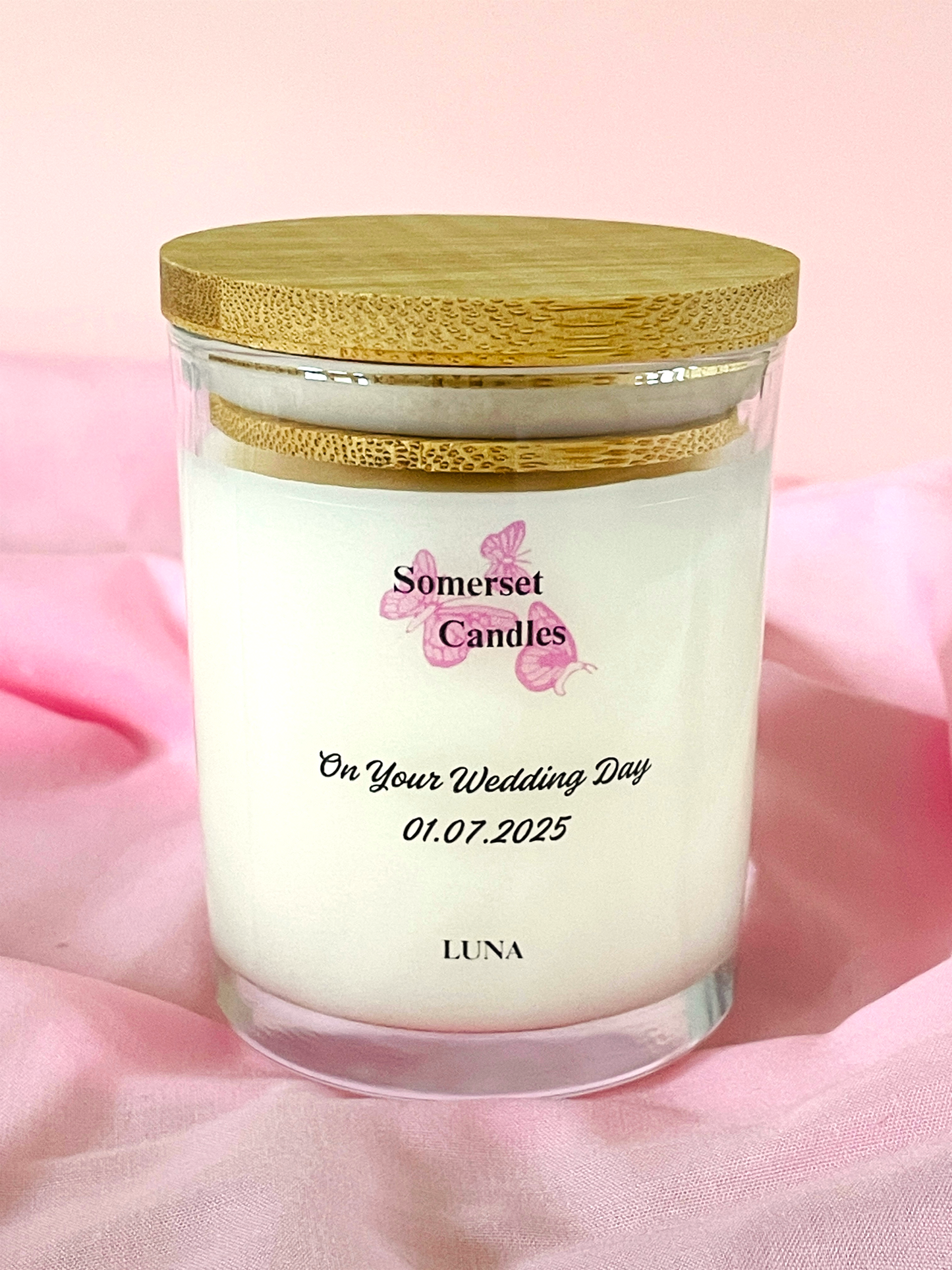 Somerset Candles wedding-themed candle with a wooden lid on a pink fabric background