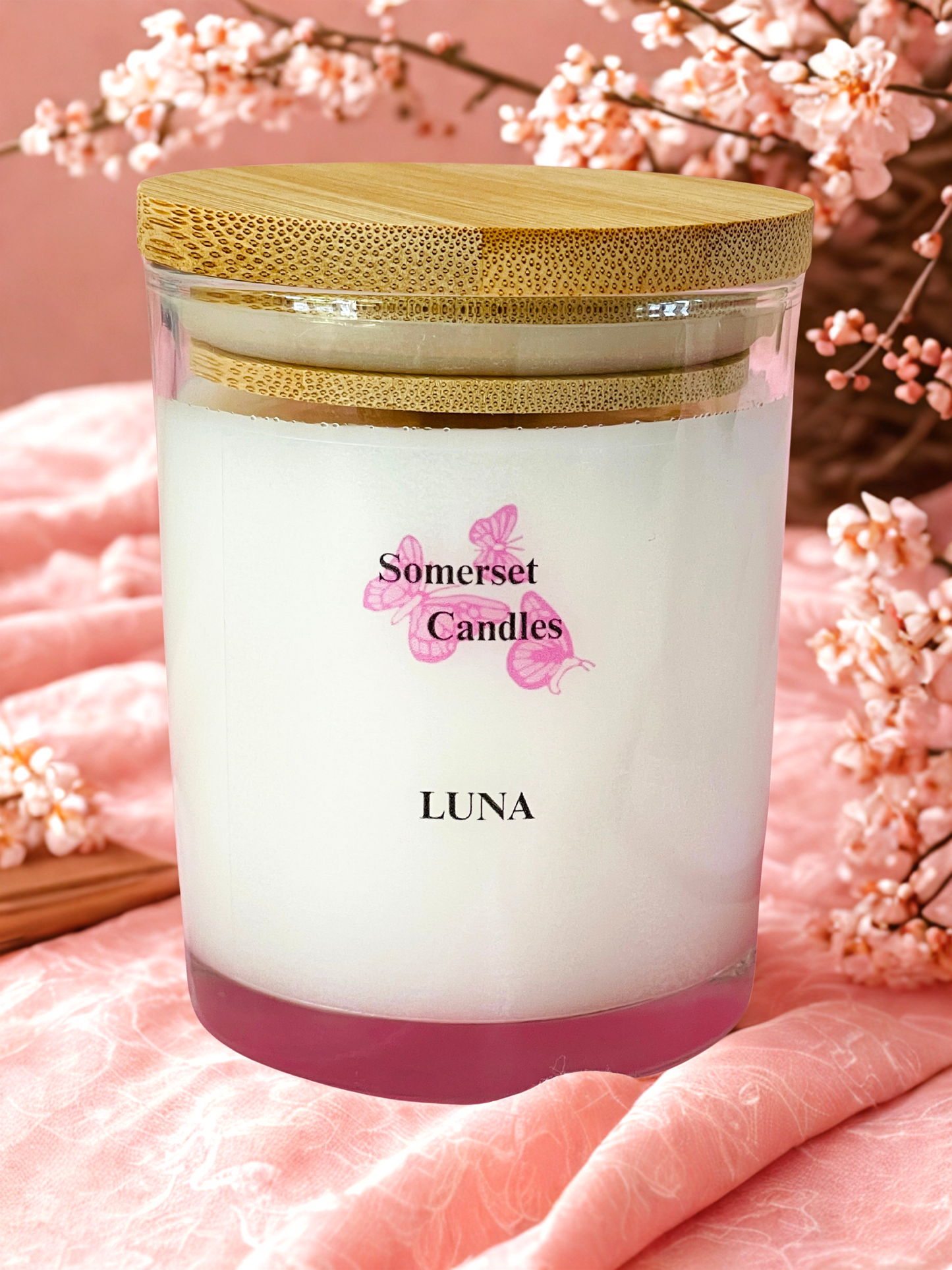 Somerset Candles Luna candle with a wooden lid on a pink background with cherry blossoms.