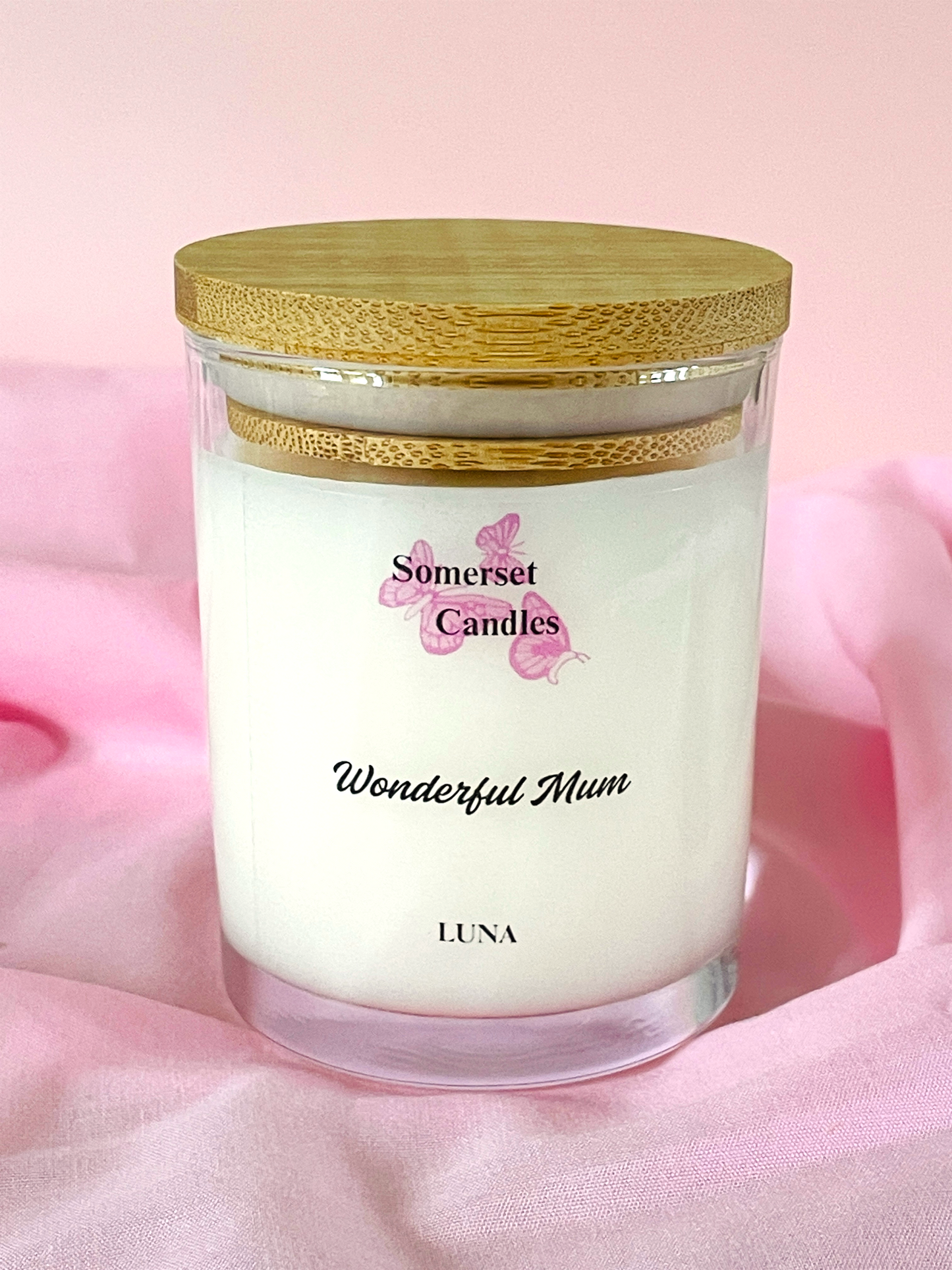 Candle in a glass jar with a wooden lid on a pink background, featuring the brand 'Somerset Candles'.