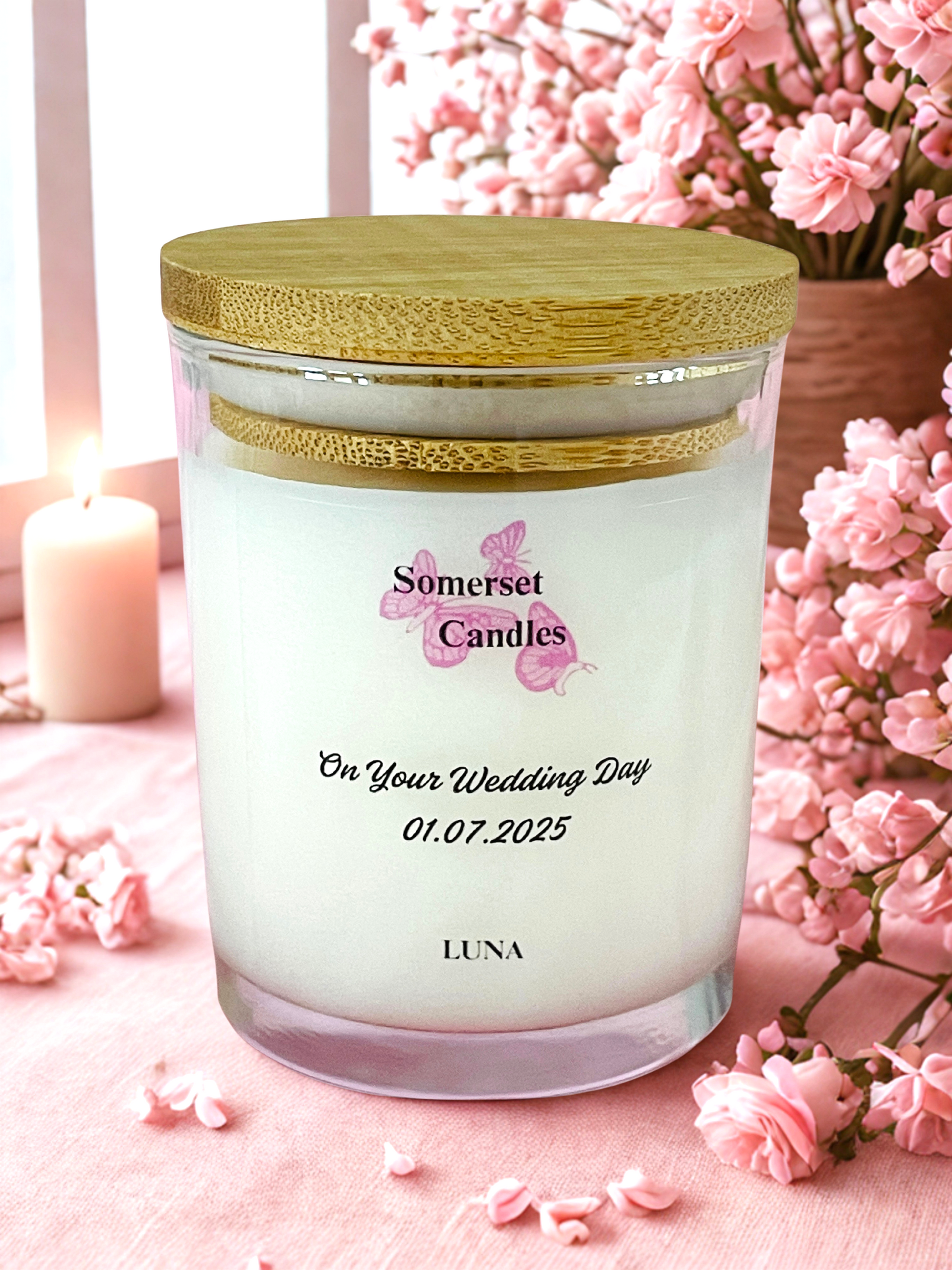 Personalised candle with floral design and text on a pink surface with flowers.